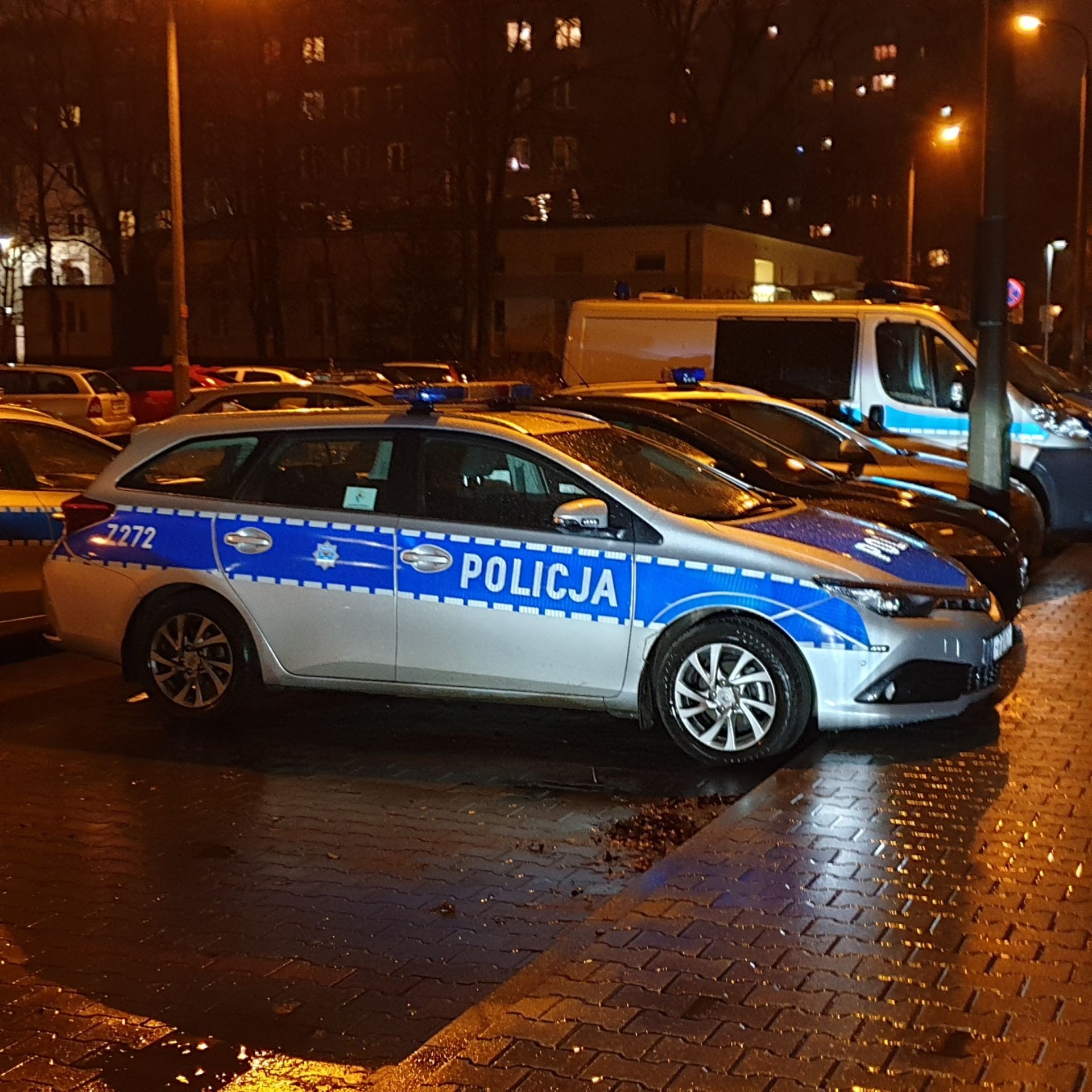 Radiowóz policyjny zaparkowany nocą na mokrej ulicy — symbol sankcji dyscyplinarnych wobec policjanta.