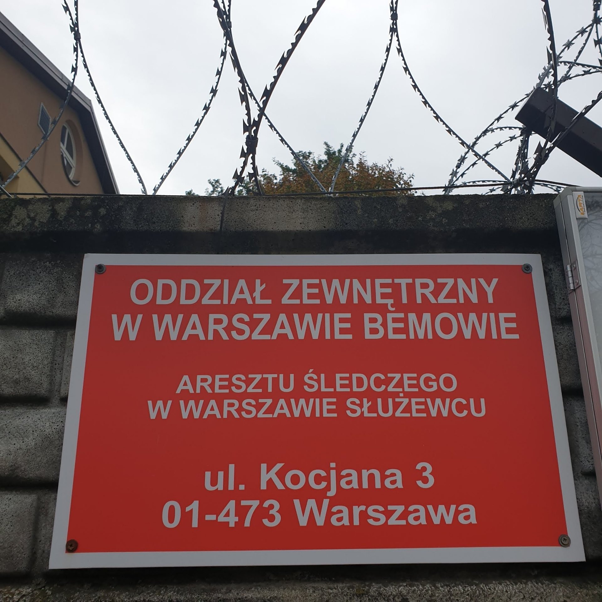Tablica Oddziału Zewnętrznego Aresztu Śledczego w Warszawie pod zwojami concertiny — symbol sankcji dyscyplinarnych wobec funkcjonariusza Służby Więziennej.
